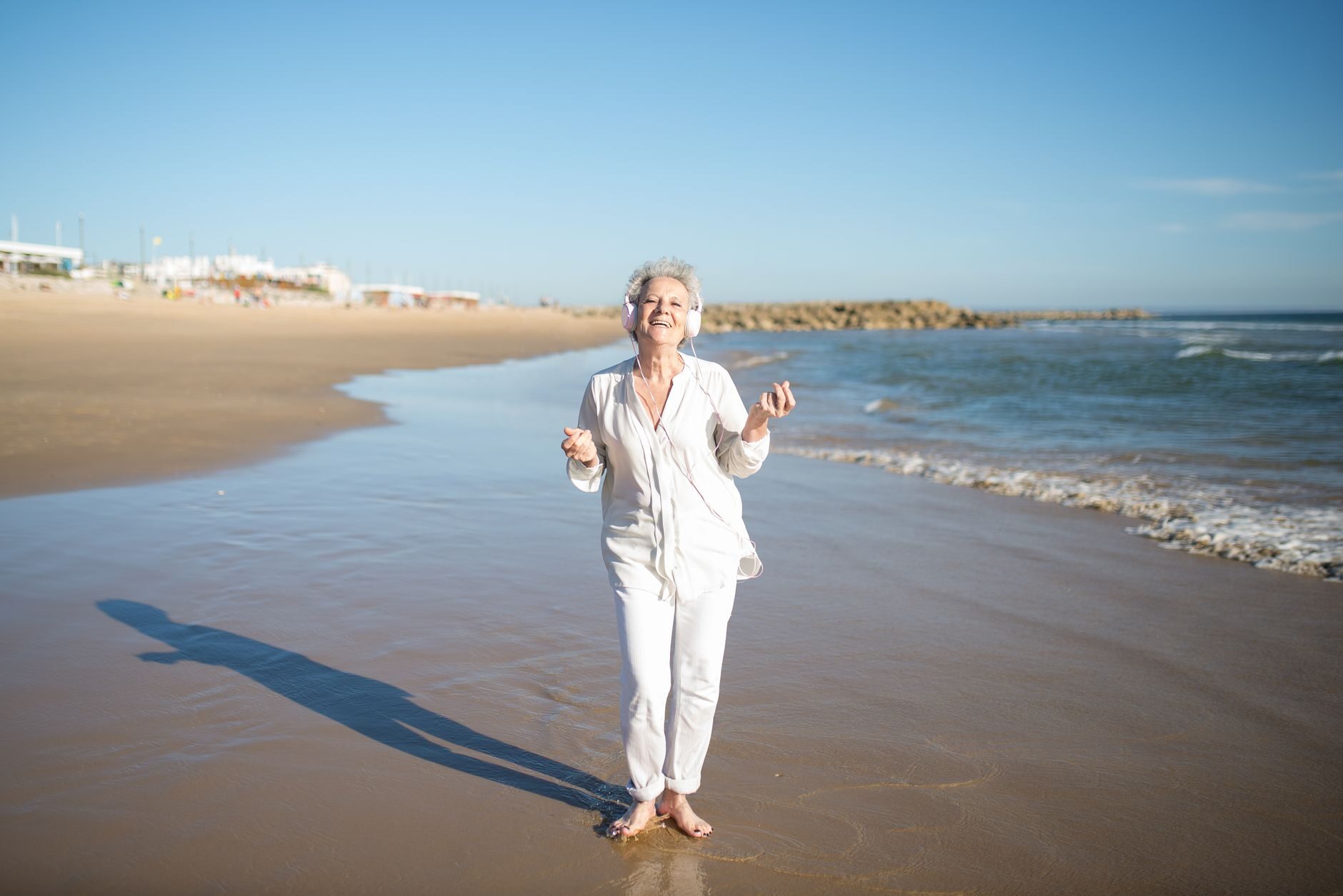 A vibrant woman in white standing radiant at the shoreline with a broad, genuine smile