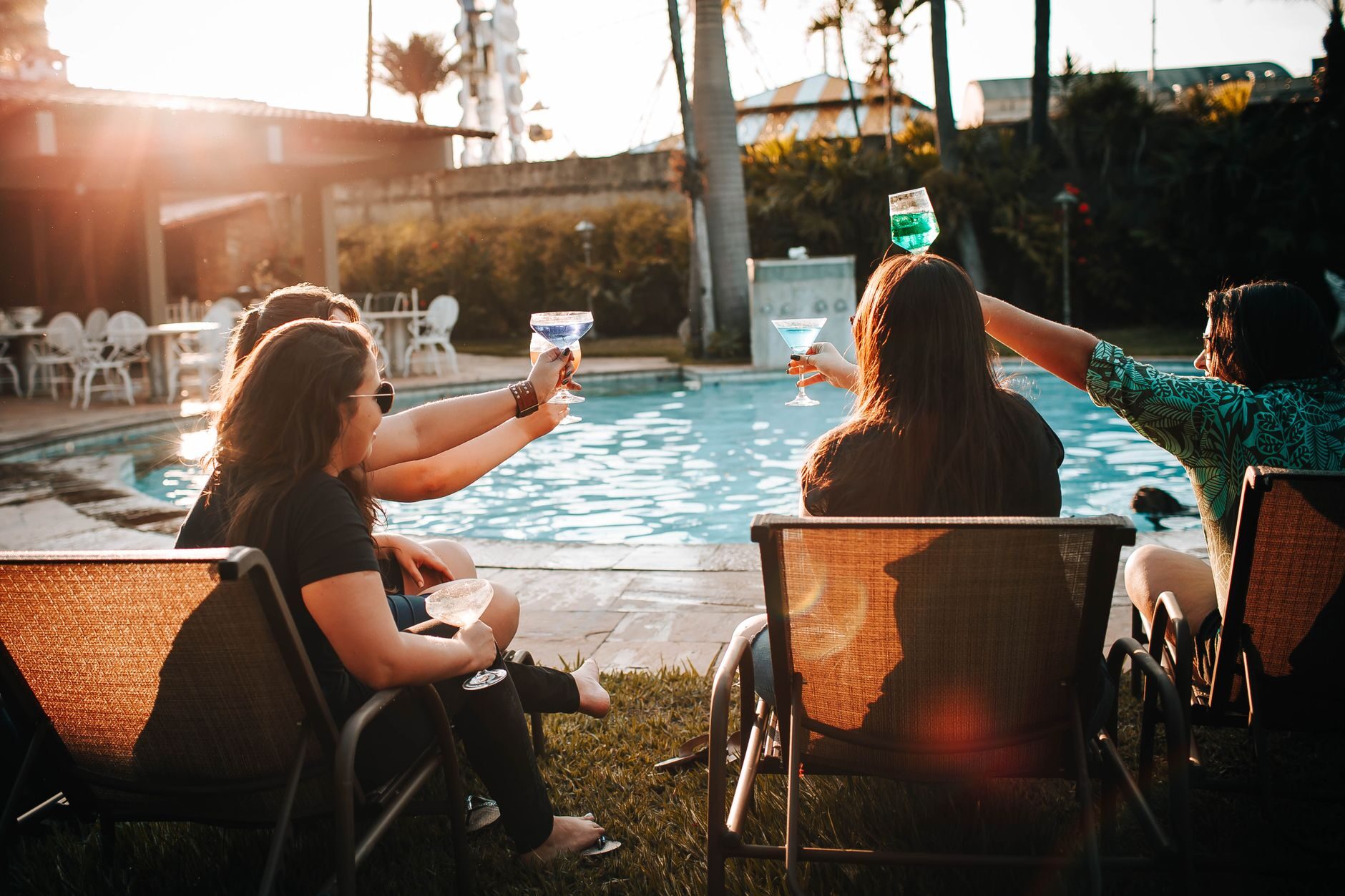 A group raising a toast at golden-hour poolside with palms backlit behind them